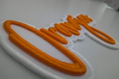 白い生地にオレンジ色の糸で加工された3D文字刺繍ワッペンのアップ。