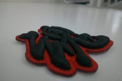 ベースを赤糸で刺繍し黒糸で文字を刺繍した迫力のある3D刺繍ワッペンの別角度からのアップ。