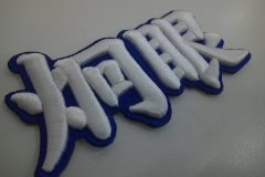青のエンブクロス生地を土台に、白糸で炯眼の文字を太めに刺繍した、3D刺繍ワッペンの制作事例。