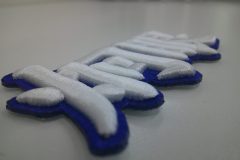 青のエンブクロス生地を土台に、白糸で炯眼の文字を太めに刺繍した、3D刺繍ワッペンの制作事例。横からのアングル。