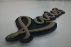 黒のベース生地にブラウンベージュでチーム名を加工した、オリジナル3D刺繍ワッペンの加工実績。横からの撮影。