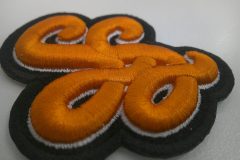 黒のエンブクロス生地をベースに濃いめのオレンジ糸と白糸でSSのロゴ文字を3D刺繍ワッペンとして加工した事例。