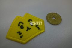 黄色い生地で猫の形を模って黒糸で顔を刺繡した、オリジナル刺繡ワッペンの制作実績。