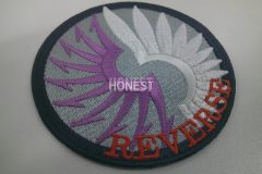 グレーの生地に白と紫の糸でモチーフを刺繡した、オリジナル刺繡ワッペンの制作実績。