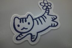 白色の生地に青色一色でしっぽにお花が咲いている猫の刺繡をしたオリジナル刺繡ワッペンの制作実績。