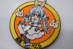 オレンジ色の生地の中心に女の子キャラクターの全身と左右にウサギの顔が刺繍されたオリジナル刺繡ワッペンの制作実績。