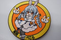 オレンジ色の生地の中心に女の子キャラクターの全身と左右にウサギの顔が刺繍されたオリジナル刺繡ワッペンの制作実績。