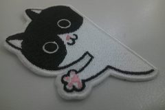 猫が壁からひょっこりと顔と手を出したようなデザインのオリジナル刺繡ワッペンの制作実績。。