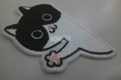 猫が壁からひょっこりと顔と手を出したようなデザインのオリジナル刺繡ワッペンの制作実績。。