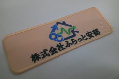 ベージュの生地に会社ロゴを刺繡した、長方形のオリジナル刺繡ワッペンの制作実績。