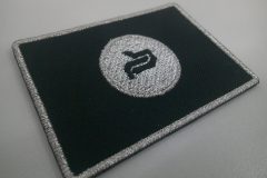 黒色の生地に銀糸で国旗と中心にロゴマークを刺繡した、オリジナル刺繡ワッペンの制作実績。