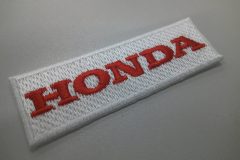 白色のクロス生地に赤い刺繍糸でメーカー名を刺繡した、オリジナル刺繡ワッペンの制作実績。