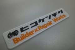 白色のクロス生地に、黒とオレンジ色で会社名を刺繡した、オリジナル刺繡ワッペンの制作実績。