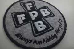 薄杢グレーのフェルト生地に黒と白色でロゴマークを刺繡した、オリジナル刺繡ワッペンの制作実績。
