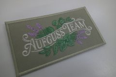 グレージュの生地に柔らかい色合いの草花とチーム名を刺繡した、オリジナル刺繡ワッペンの制作実績。