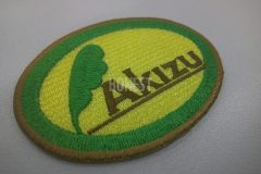 黄色い生地に緑色の羽と円で茶色の社名を囲んだ刺繍をした、オリジナル刺繡ワッペンの制作事例。