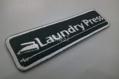 黒色の生地に白糸で店名としわをアイロンで伸ばしたようなイラストを刺繡した、オリジナル刺繡ワッペンの制作事例。
