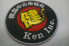 赤い生地に黒色で太い縁を縫いその上に白糸で会社名と、真ん中に漢字の一部がトラのしっぽになった一文字を黄色で刺繡した、オリジナル刺繡ワッペンの制作事例。