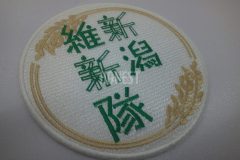 白色のクロス生地に緑色で団体名を真ん中に、黄金色の稲穂で円を縁取るような刺繡をした、オリジナル刺繡ワッペンの制作事例。