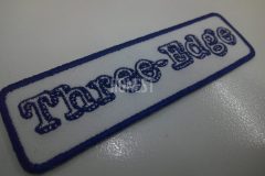白色の生地に、ネイビーの糸で変わったアルファベットの文字デザインで名前を刺繡した、オリジナル刺繡ワッペンの制作事例。