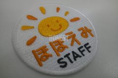 白色の生地にオレンジと濃い黄色で太陽のイラストを刺繡した、スタッフオリジナル刺繡ワッペンの制作実績。
