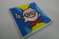 黄色い生地に青と水色で描いた二つの半円の上に眼鏡をかけた胃のキャラクターを刺繡した、オリジナル刺繡ワッペンの制作事例。