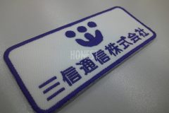 白色の生地に濃い青色で会社ロゴと会社名を二段で刺繡した、オリジナル刺繡ワッペンの制作事例。