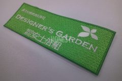 緑のナイロンエンブクロスをベースにホワイト単色で建設会社のロゴを刺繍したオリジナルワッペンの制作事例。