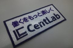 白の生地をベースに紫の糸で社名と社訓を二段で加工した文字ワッペンの制作事例。