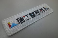 白のエンブクロス生地をベースに整形外科のロゴを刺繍加工したオリジナル刺繍ワッペンの制作実績。