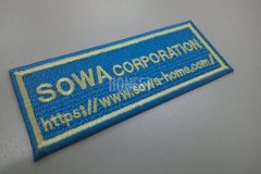ターコイズブルーの生地をベースにライトイエロー単色で社名とURLを刺繍した、社名ワッペンの制作事例。