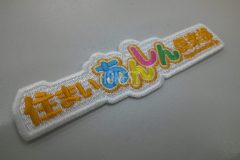 白のエンブクロス生地に華やかな多色で建設会社のオリジナルロゴを刺繍ワッペンとして縫い上げた高級感あふれる仕上がりを示す事例。