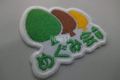 白のツイル生地に社会福祉法人のロゴを刺繍したオリジナル刺繍ワッペン。緑色・茶色・山吹色・白の4色構造。