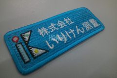 エメラルドカラーのエンブクロス生地に測量会社のロゴを加工した、企業ロゴ刺繍ワッペンの制作実例。