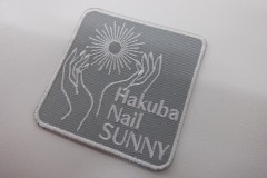 ネイルを施した手を太陽の光に向けたイラストと店名を刺繡したオリジナル刺繡ワッペンの制作実績。
