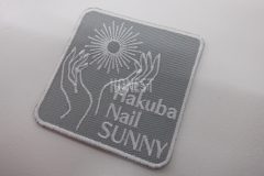 ネイルを施した手を太陽の光に向けたイラストと店名を刺繡したオリジナル刺繡ワッペンの制作実績。