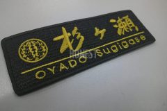 黒のエンブクロス生地にマットゴールドの糸色で日本旅館のオリジナルロゴを刺繍したワッペンの制作事例。