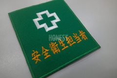 緑のフェルト生地に安全マークと安全衛生担当者の文字をシンプルに刺繍した長方形のワッペン。