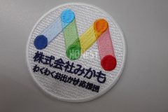 青、水色、緑、オレンジ、赤のグラデーションを綺麗に表現したロゴと、会社名を刺繡した、オリジナル刺繡ワッペンの制作実績。