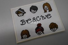 白色の生地に六人の男女の顔と中心部に店舗名を刺繍した、オリジナル刺繡ワッペンの制作事例。