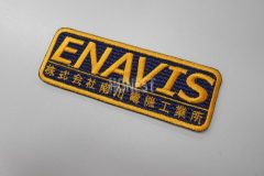 黒色のクロス生地にオレンジ色の糸で会社名を二行で刺繡した、オリジナル刺繡ワッペンの制作事例。