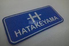 青色のクロス生地に白糸で上段にマークを、下段に名前を刺繡した、オリジナル刺繡ワッペンの制作事例。