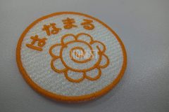 白色の生地にオレンジ色の糸ではなまるの文字と花丸マークを刺繡した、オリジナル刺繡ワッペンの制作事例。