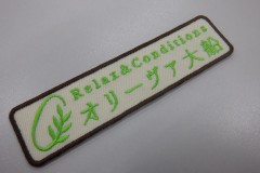 クリーム色の生地に明るい黄緑の糸でオリーブの葉をイメージしたマークと店舗名を刺繡した、オリジナル刺繡ワッペンの制作実績。