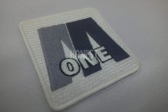 白色のツイル生地に黒とグレーの糸でロゴマークを刺繡したオリジナル刺繡ワッペンの制作事例。