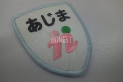 白色のツイル生地に濃ピンク、薄ピンク、緑でロゴを刺繡した、オリジナル刺繡ワッペンの制作事例。