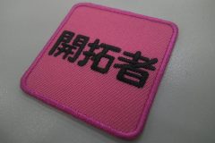 発色性の良いピンクの生地に黒糸で「開拓者」と刺繍した、もったいないワッペン。書体は丸ゴシックを使用。