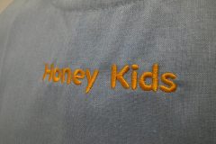 水色のエプロンの胸元中央部分に保育園名を英字でネーム刺繡した制作事例のアップ。
