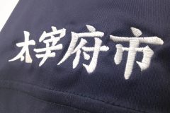 紺色の競技チームのユニフォームシャツの右袖に白糸で文字刺繍をした制作事例のアップ。