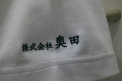 白Tシャツの左袖に漢字の企業名を黒糸で刺繡した制作事例のアップ。